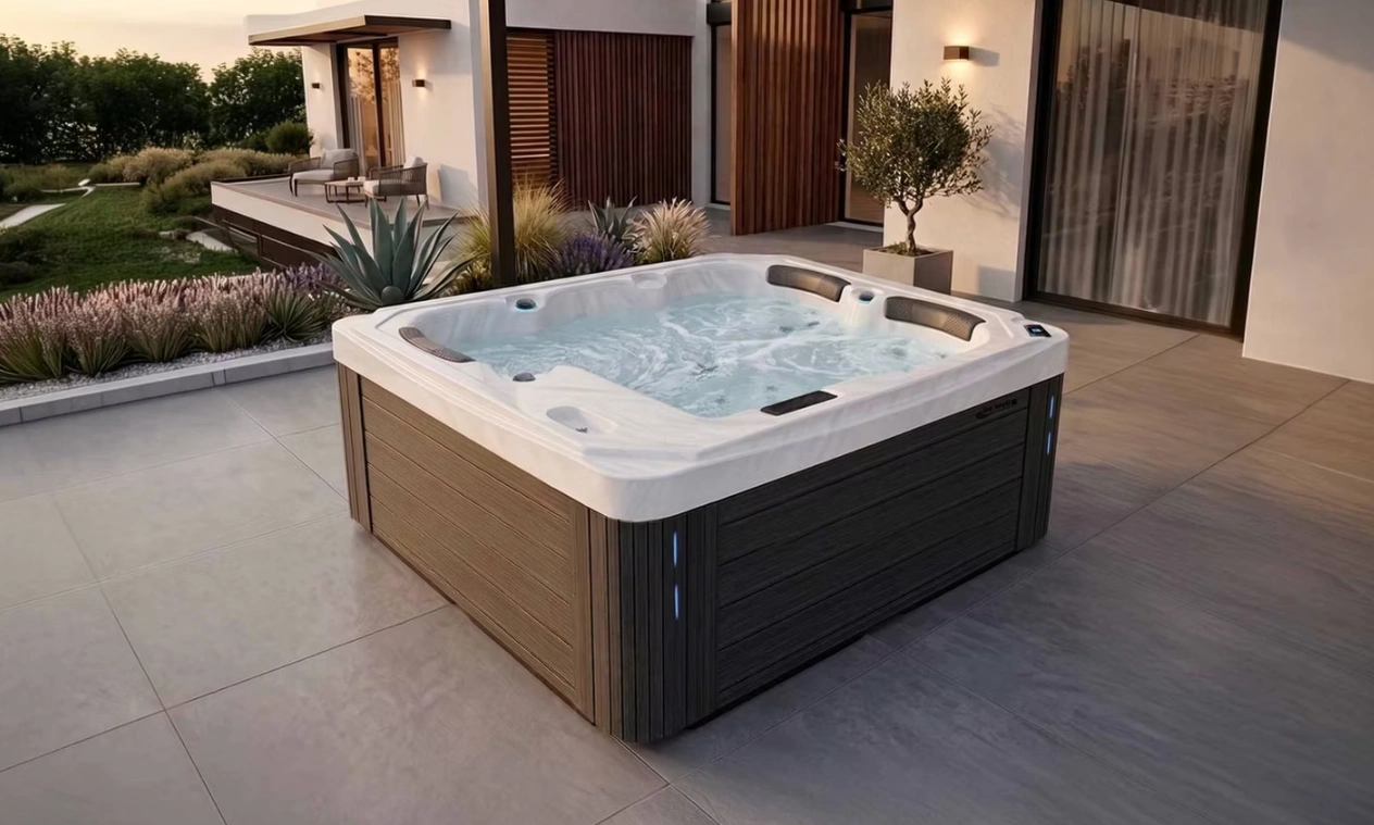 Be Well Canada spa on a modern stone patio with wood-grain cabinet, surrounded by landscaping and a contemporary home